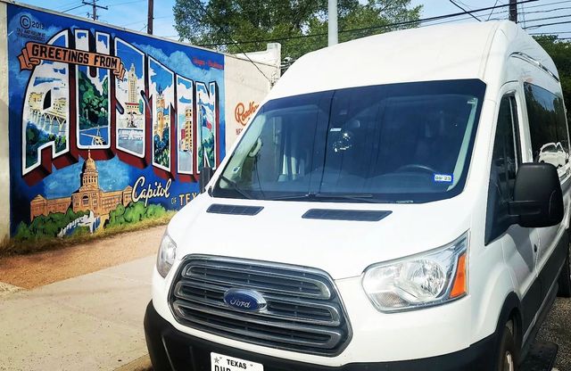 White Ford Transit van parked beside colorful Greetings from Austin mural depicting the Texas Capitol, street scene in Austin, Texas