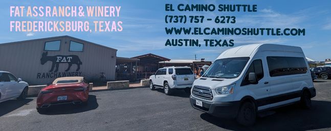 Rustic winery parking lot in Fredericksburg, Texas — barn-style tasting room, parked cars and a white shuttle van under a bright blue sky.
