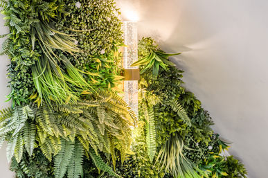 Lush indoor vertical green wall of ferns, ornamental grasses, and foliage glowing under a modern glass wall sconce with warm light