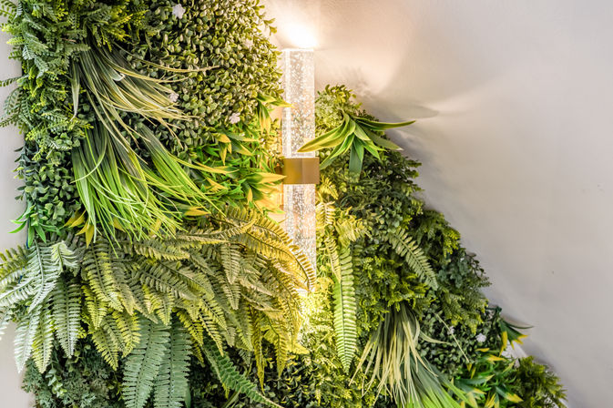 Lush indoor vertical green wall of ferns, ornamental grasses, and foliage glowing under a modern glass wall sconce with warm light