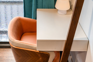 Cozy modern desk nook with a peach-orange upholstered chair, white floating desk and small lamp by a teal curtain, patterned privacy window film and wood accents.