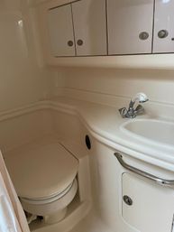 Compact beige boat bathroom (marine head) with molded fiberglass sink and counter, chrome faucet, overhead storage cabinets and a closed marine toilet