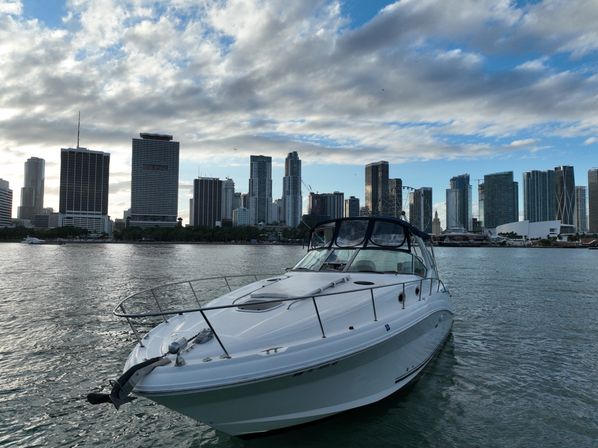 White cabin cruiser on Biscayne Bay with downtown Miami skyline and a ferris wheel under a dramatic cloudy blue sky