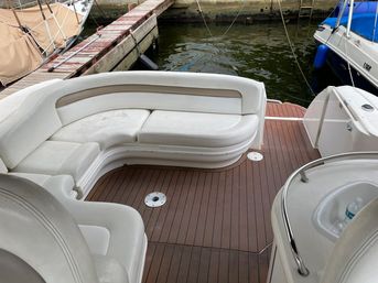 Cozy curved white vinyl bench on a teak boat deck at a marina, dockside water and neighboring boats visible.
