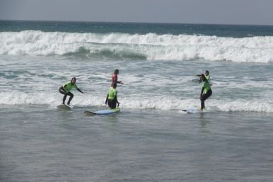 Surfing lesson: four beginners in bright green rashguards on foam surfboards catching small ocean waves at a sandy beach