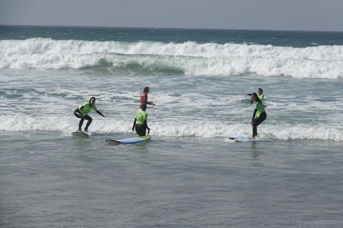 Surfing lesson: four beginners in bright green rashguards on foam surfboards catching small ocean waves at a sandy beach