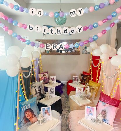 Indoor pastel birthday sleepover in a living room with canopy tents, balloon garlands spelling "in my birthday era", fairy lights, lanterns and pop‑singer album-style pillows on low tables.