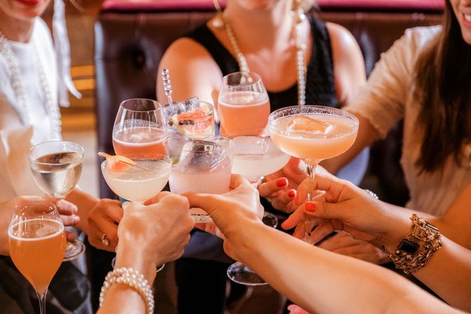 Friends clinking assorted pink and citrus cocktails in stemmed glasses during a festive brunch or cocktail bar celebration