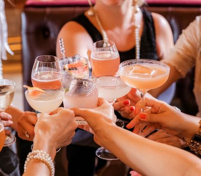 Friends clinking assorted pink and citrus cocktails in stemmed glasses during a festive brunch or cocktail bar celebration
