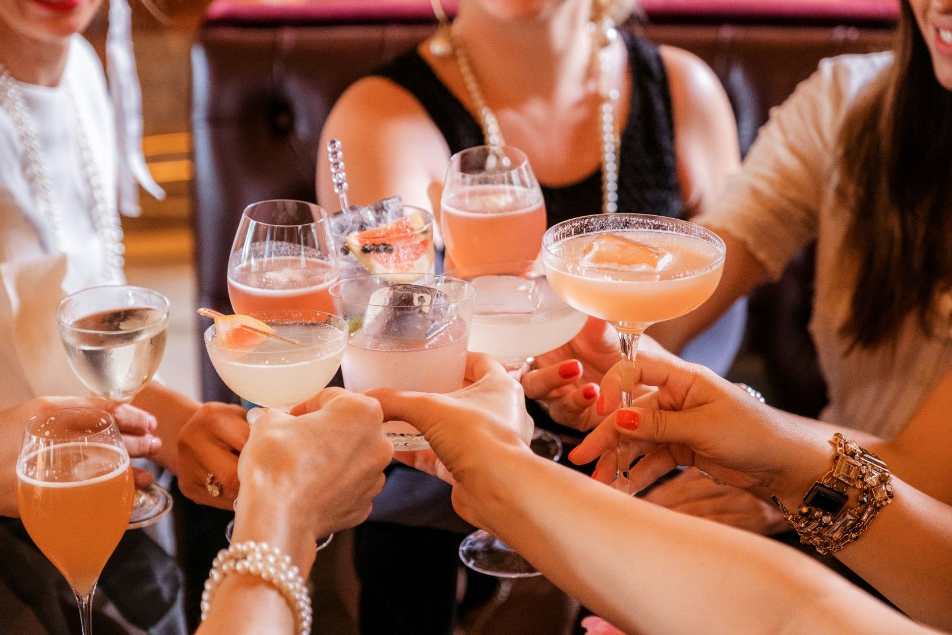 Friends clinking assorted pink and citrus cocktails in stemmed glasses during a festive brunch or cocktail bar celebration