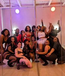 Group of women posing in lingerie and fishnet outfits around mirrored pole dance poles in a pink‑purple lit studio — playful pole dance party or girls' night celebration.
