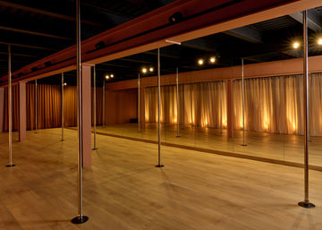 Boutique pole fitness studio interior with chrome poles, floor-to-ceiling mirrors, light wood flooring and warm curtain uplighting