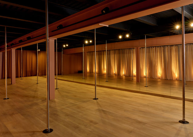 Boutique pole fitness studio interior with chrome poles, floor-to-ceiling mirrors, light wood flooring and warm curtain uplighting