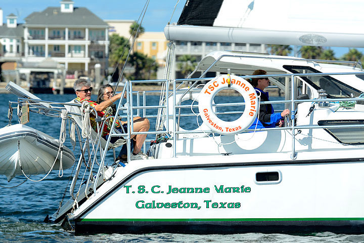 Two people relaxing on the stern of a white sailboat with a life ring and dinghy, waterfront homes in the background, Galveston, Texas
