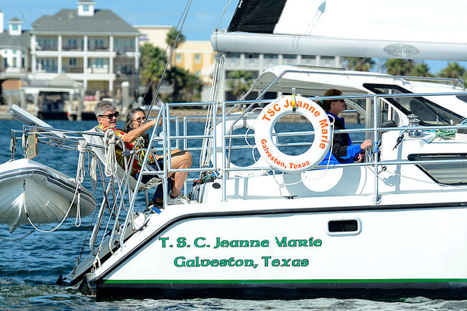 Two people relaxing on the stern of a white sailboat with a life ring and dinghy, waterfront homes in the background, Galveston, Texas