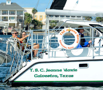 Two people relaxing on the stern of a white sailboat with a life ring and dinghy, waterfront homes in the background, Galveston, Texas