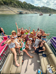 Sunny summer lake party on a pontoon boat — a joyful group of adults in swimsuits raising drinks and smiling on clear water with rocky shoreline and docks in the background.