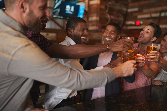 Group of friends clinking beer glasses over a rustic bar counter, laughing and toasting for a lively night out.