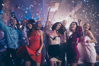 Festive nightclub scene: friends dancing on a crowded dance floor under colorful lights and falling confetti, cheering and laughing.