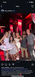 Group of seven friends posing and smiling in a red-lit Las Vegas nightclub with draped curtains; women wearing short white and lavender party dresses and platform shoes, men in casual shirts — festive bachelorette-style celebration.