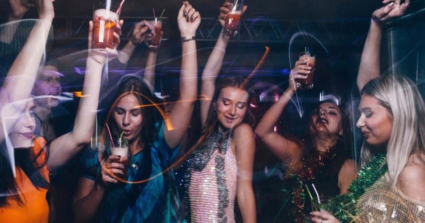 Group of friends dancing and raising cocktails on a lively nightclub dance floor under colorful lights