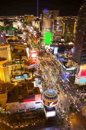 Aerial night view of the Las Vegas Strip with glittering hotels, neon signs, colorful billboards and steady traffic along the bustling, brightly lit boulevard.