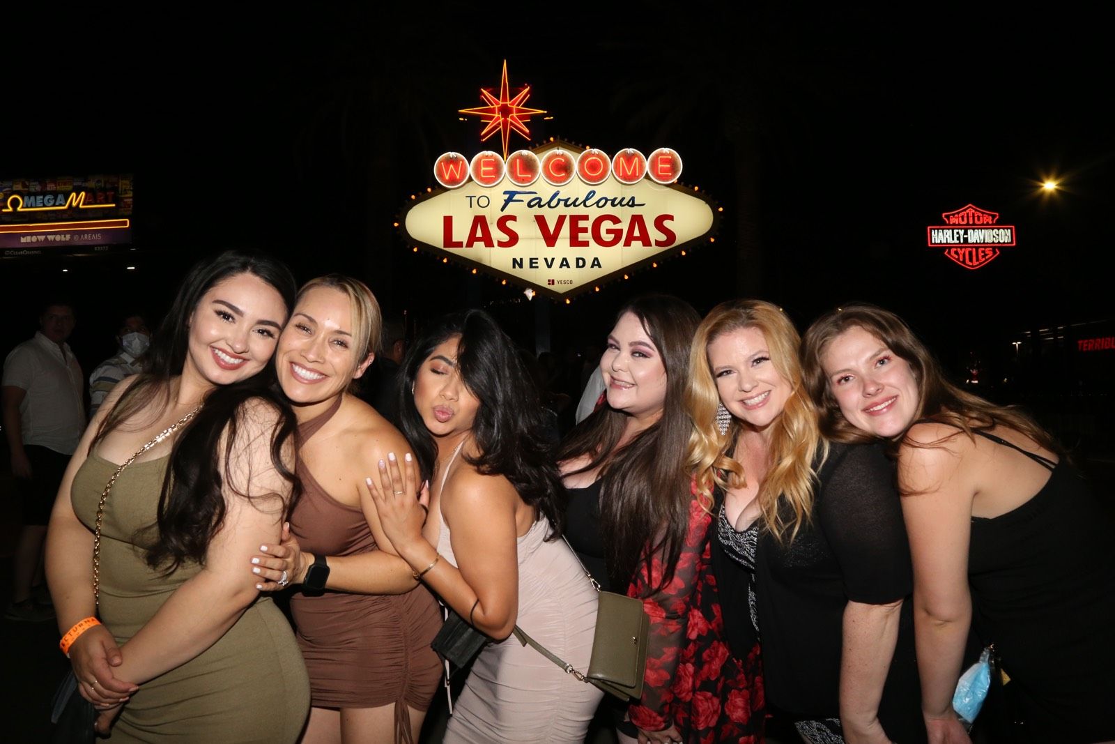 Group of women posing and smiling at night in front of the illuminated "Welcome to Fabulous Las Vegas Nevada" sign on the Las Vegas Strip