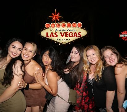 Group of women posing and smiling at night in front of the illuminated "Welcome to Fabulous Las Vegas Nevada" sign on the Las Vegas Strip