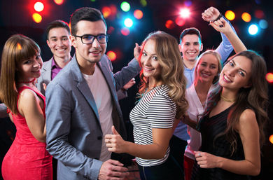 Smiling young adults dancing and posing together at a lively nightclub party with colorful blurred lights in the background