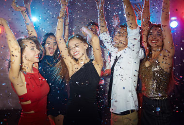 Group of friends dancing and celebrating under colorful nightclub lights with confetti falling on a lively dance floor — energetic downtown nightlife scene.