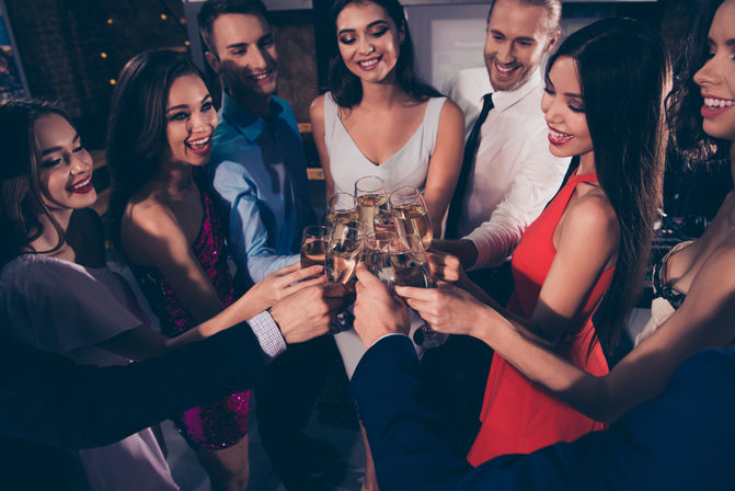 Cheerful group of well-dressed friends toasting with champagne flutes at an indoor evening party or bar, smiling as they clink glasses.
