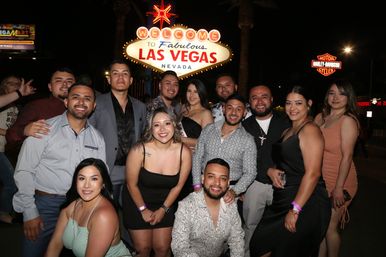 Smiling group of friends in evening outfits posing at night under the illuminated "Welcome to Fabulous Las Vegas, Nevada" sign