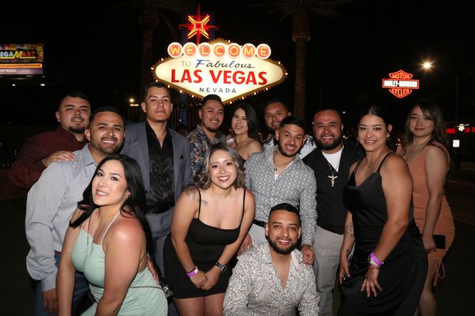 Smiling group of adults posing at night in front of the illuminated Welcome to Fabulous Las Vegas Nevada sign on the Strip, palm trees and city lights in the background