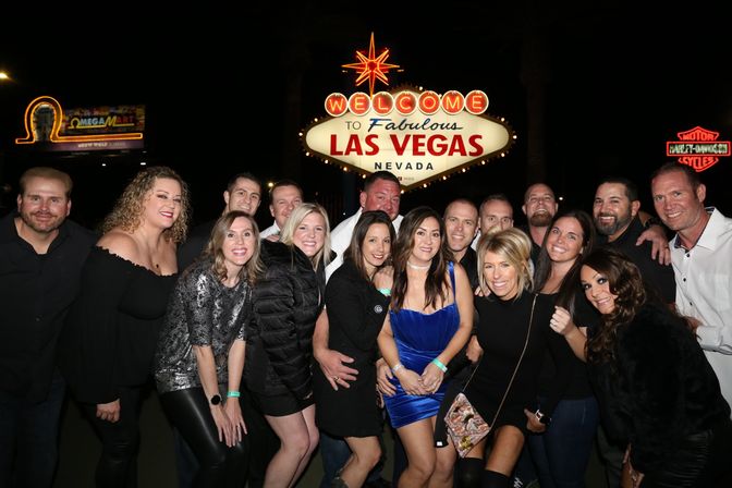 Cheerful group of friends posing at night in front of the iconic "Welcome to Fabulous Las Vegas Nevada" sign, dressed for a night out on the Las Vegas Strip.