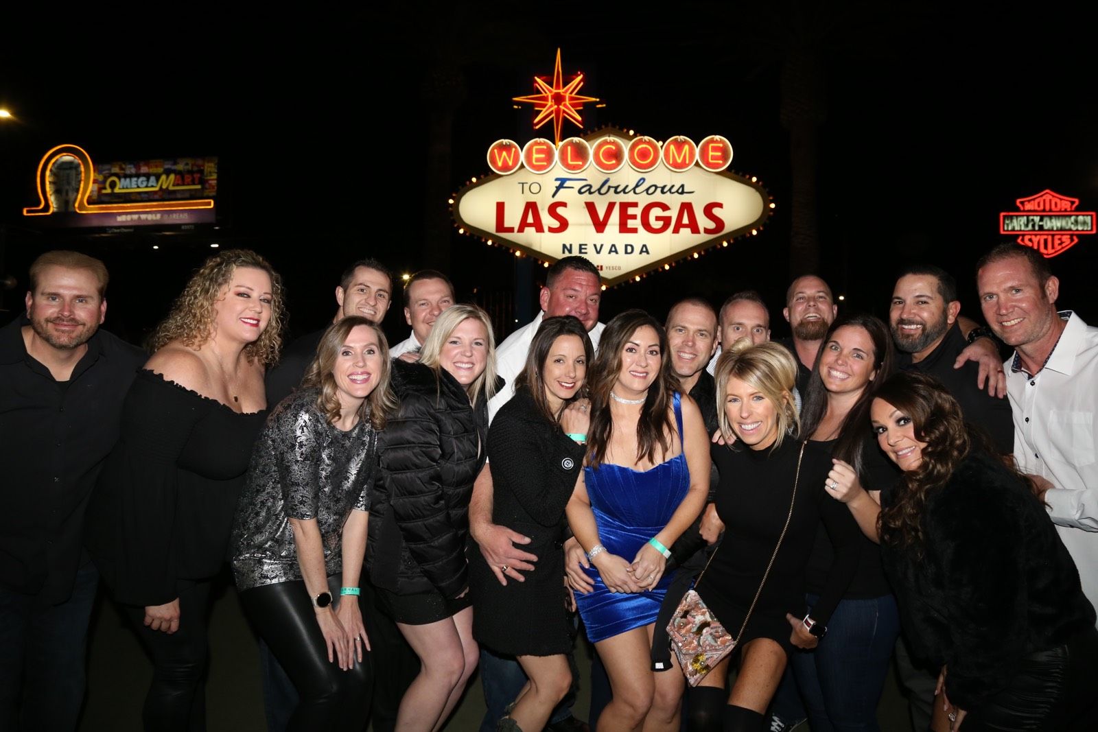 Cheerful group of adults posing at night in front of the illuminated "Welcome to Fabulous Las Vegas Nevada" sign on the Las Vegas Strip.