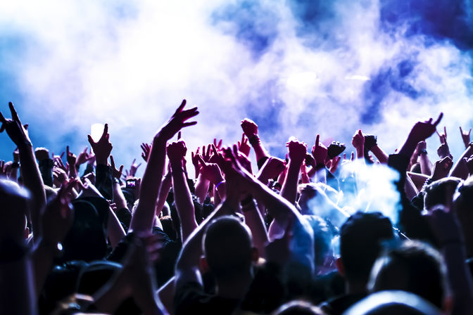 Energetic live music crowd with hands raised, glowing purple-blue stage lights and smoky atmosphere