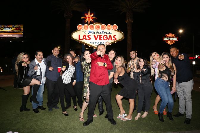 Party group playfully posing and pointing at camera in front of the illuminated "Welcome to Fabulous Las Vegas, Nevada" sign at night with palm trees