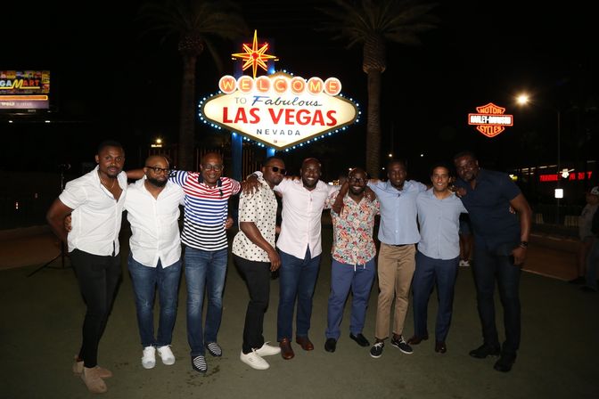 Group of men posing at night in front of the iconic Welcome to Fabulous Las Vegas, Nevada sign with palm trees and neon lights in the background.