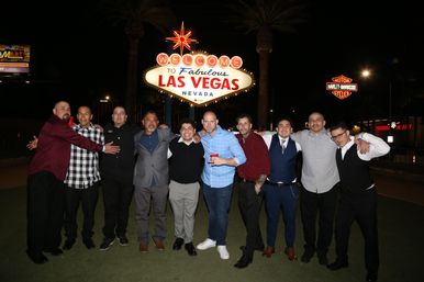 Group of men posing at night in front of the illuminated "Welcome to Fabulous Las Vegas Nevada" sign on the Las Vegas Strip