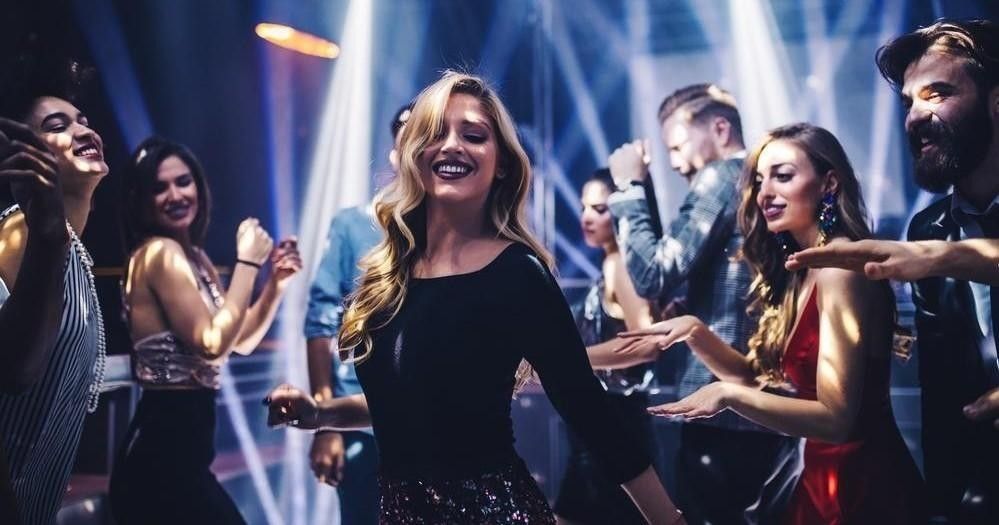 Group of people dancing on a lively city nightclub dance floor, smiling under colorful spotlights and glittering outfits