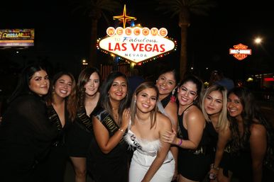 Cheerful group of women posing at night in front of the illuminated "Welcome to Fabulous Las Vegas Nevada" sign with palm trees and neon lights