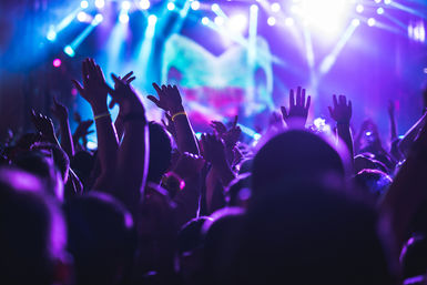 Energetic live concert crowd with hands raised under vivid purple and blue stage lights and spotlights, lively music festival nightlife atmosphere