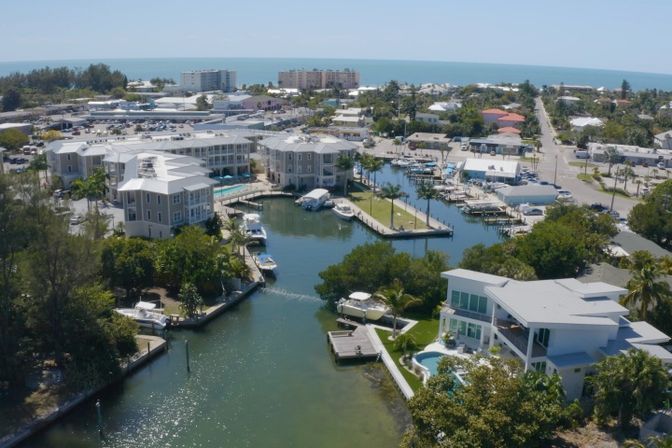 Aerial view of a sunny coastal canal neighborhood with waterfront homes, private docks and boats leading to the ocean horizon.