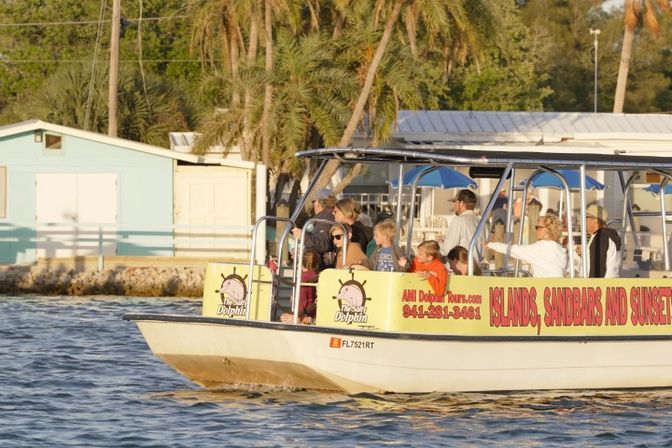 Sightseeing tour boat with families cruising along a Florida shoreline at sunset, palm trees and pastel waterfront cottages in the background.
