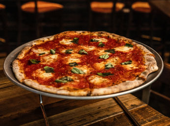 Thin-crust Margherita pizza with bright tomato sauce, melted mozzarella and fresh basil on a metal stand over a rustic wooden table in a cozy pizzeria