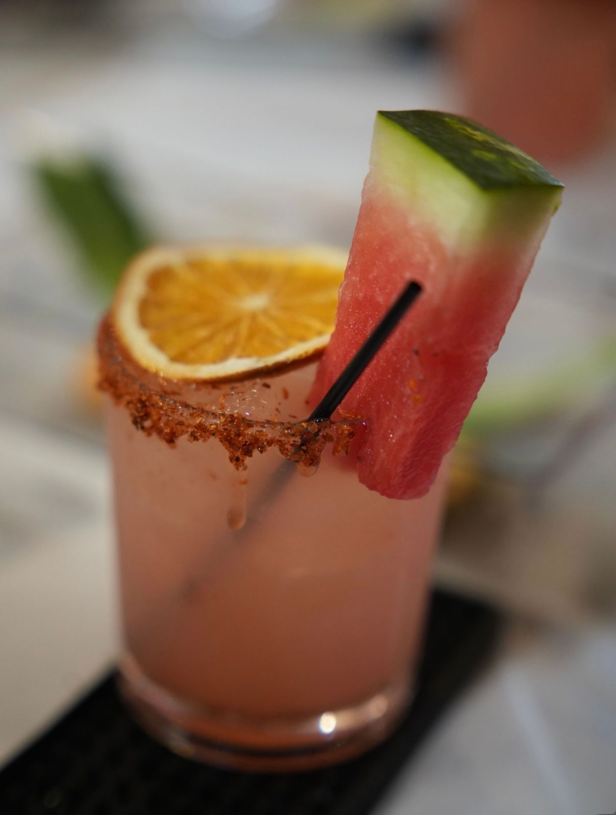 Refreshing pink watermelon cocktail in a short glass with spicy chili-salt rim, dehydrated orange slice and watermelon wedge garnish