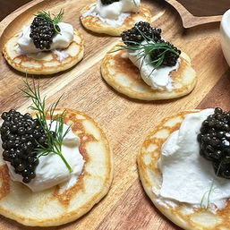 Mini golden blinis topped with creme fraiche, glossy black caviar and dill sprigs on a wooden serving board — elegant gourmet appetizers.