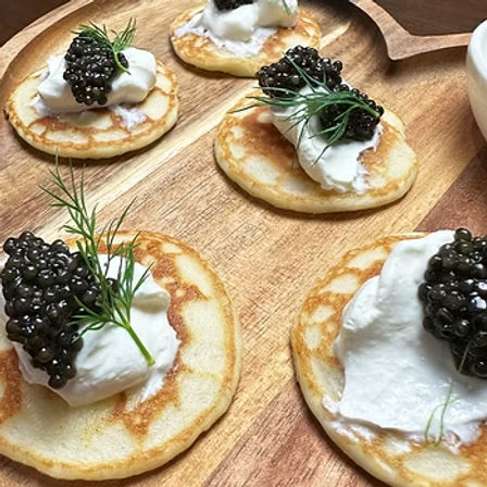 Mini golden blinis topped with creme fraiche, glossy black caviar and dill sprigs on a wooden serving board — elegant gourmet appetizers.