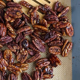 Close-up of sticky, glossy candied pecans cooling on a silicone baking mat on a baking sheet