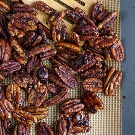 Close-up of sticky, glossy candied pecans cooling on a silicone baking mat on a baking sheet